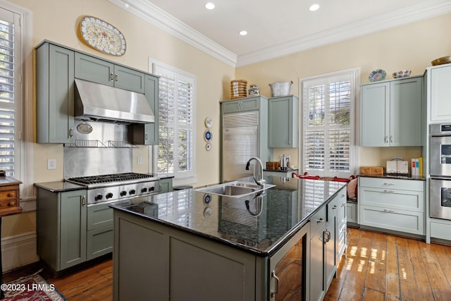 kitchen with crown molding, dark stone countertops, stainless steel appliances, an island with sink, and beverage cooler