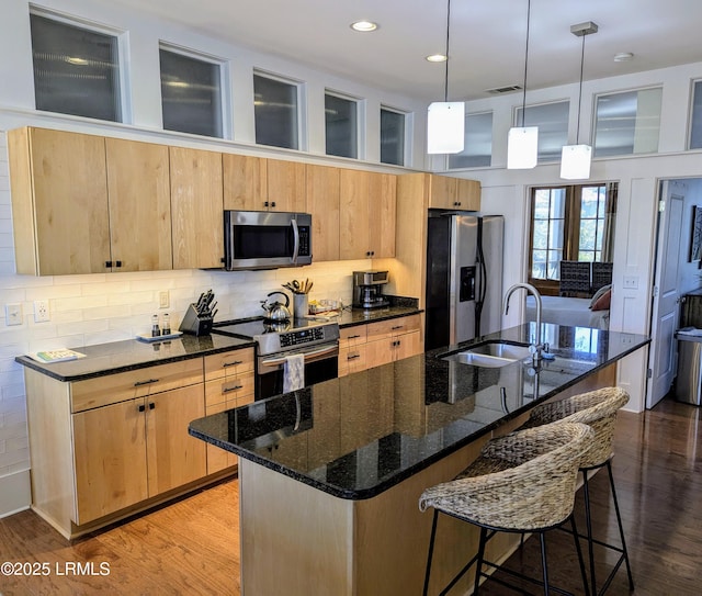 kitchen featuring appliances with stainless steel finishes, hanging light fixtures, an island with sink, sink, and dark stone countertops