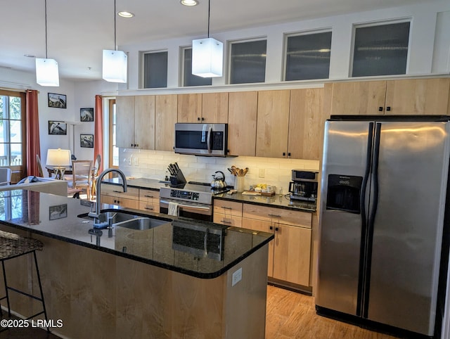 kitchen featuring an island with sink, dark stone countertops, decorative light fixtures, sink, and appliances with stainless steel finishes