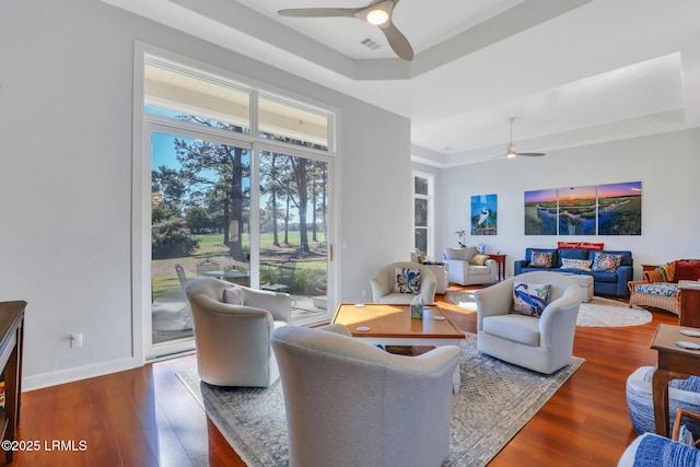 living room featuring hardwood / wood-style flooring, ceiling fan, and a tray ceiling