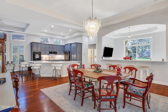 dining space with a raised ceiling, dark hardwood / wood-style floors, ceiling fan with notable chandelier, and a towering ceiling