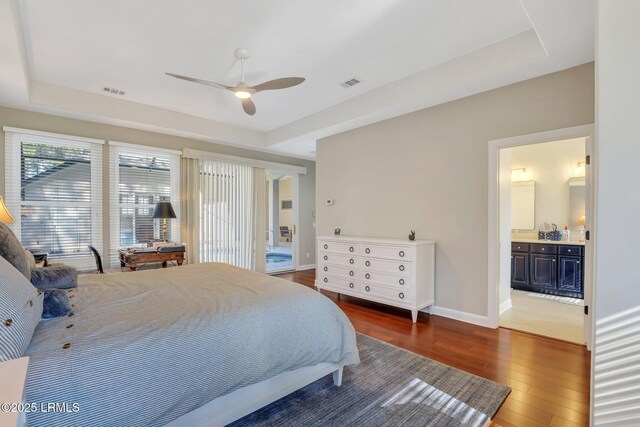 bedroom with ceiling fan, connected bathroom, dark hardwood / wood-style floors, and a raised ceiling