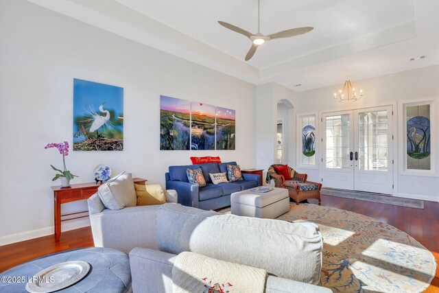 living room featuring french doors, ceiling fan with notable chandelier, dark hardwood / wood-style flooring, and a tray ceiling