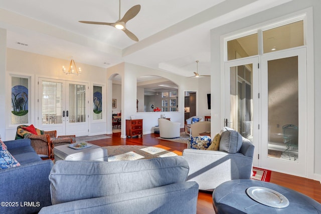 living room with hardwood / wood-style flooring, a raised ceiling, ceiling fan with notable chandelier, and french doors