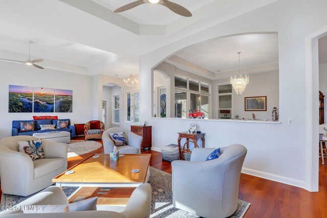 living room with dark hardwood / wood-style floors, a tray ceiling, and ceiling fan with notable chandelier