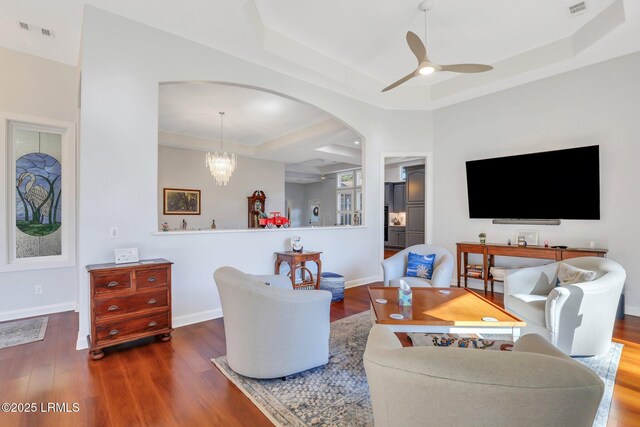 living room with a tray ceiling, wood-type flooring, and ceiling fan with notable chandelier