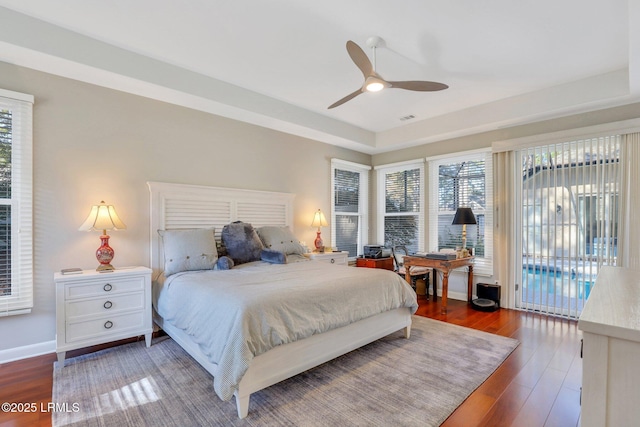 bedroom with a raised ceiling, dark hardwood / wood-style flooring, access to exterior, and ceiling fan