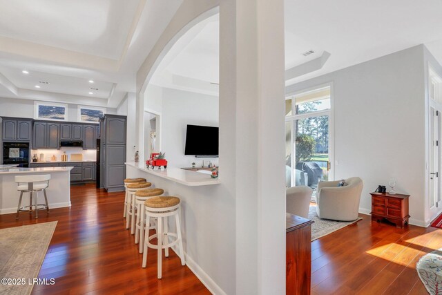 kitchen with dark hardwood / wood-style flooring, a tray ceiling, a breakfast bar, and gray cabinetry