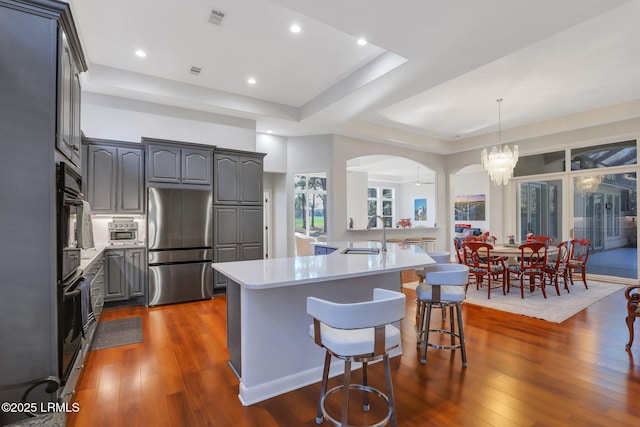 kitchen featuring sink, a breakfast bar, stainless steel refrigerator, a center island with sink, and decorative light fixtures