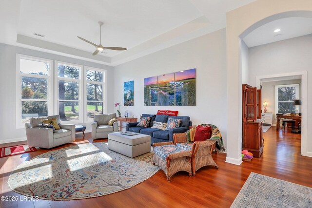 living room with dark wood-type flooring, ceiling fan, and a tray ceiling