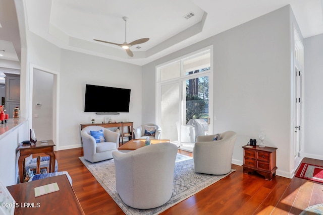 living room with ceiling fan, a tray ceiling, and dark hardwood / wood-style flooring