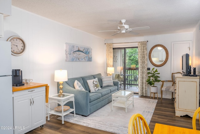 living room featuring dark wood-type flooring, ceiling fan, wooden walls, and a textured ceiling