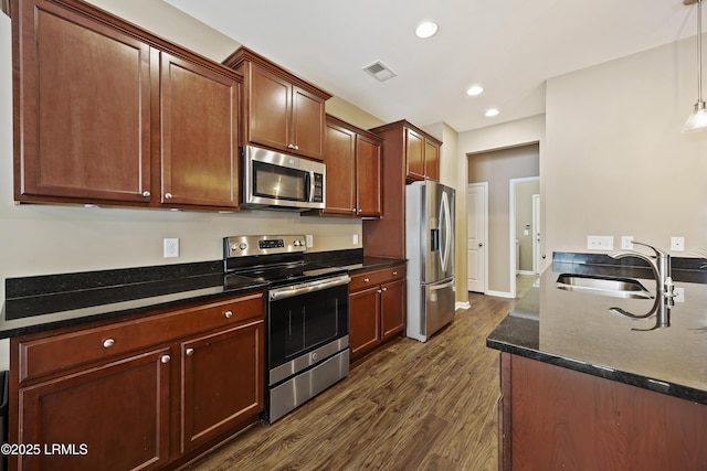 kitchen featuring sink, dark stone countertops, hanging light fixtures, stainless steel appliances, and dark wood-type flooring