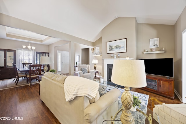 living room featuring dark wood-type flooring, lofted ceiling, a tray ceiling, and a chandelier