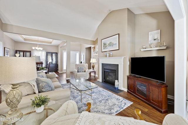 living room featuring a raised ceiling, vaulted ceiling, dark wood-type flooring, and a chandelier