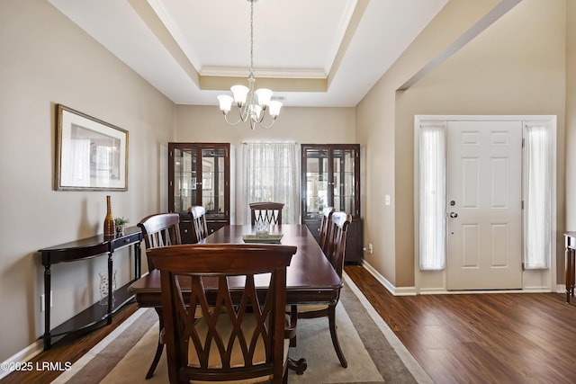 dining room with ornamental molding, dark wood-type flooring, an inviting chandelier, and a tray ceiling