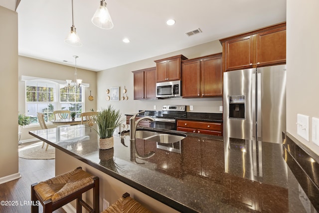 kitchen featuring sink, appliances with stainless steel finishes, a kitchen breakfast bar, decorative light fixtures, and dark stone counters