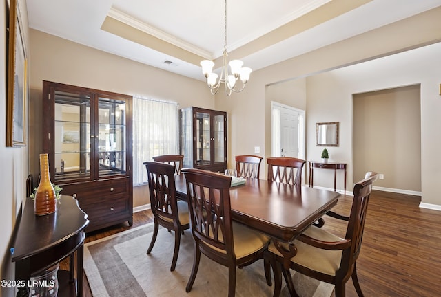 dining room with dark wood-type flooring, ornamental molding, a raised ceiling, and a notable chandelier