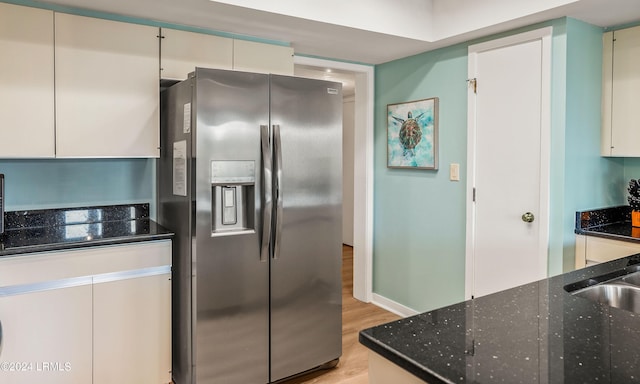 kitchen featuring sink, dark stone countertops, stainless steel refrigerator with ice dispenser, white cabinets, and light wood-type flooring