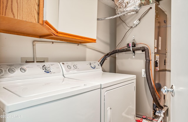 clothes washing area with cabinets, washing machine and dryer, and secured water heater