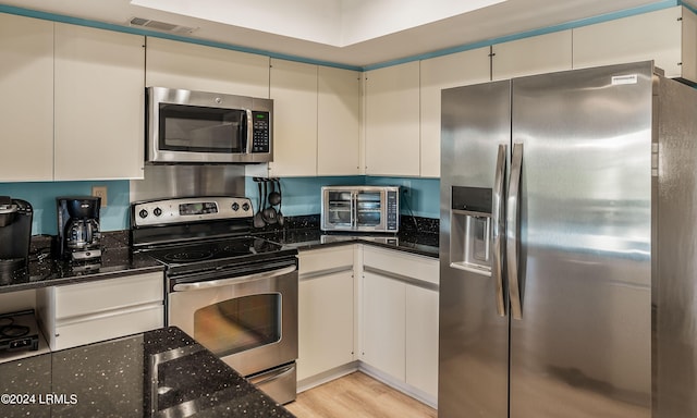 kitchen featuring white cabinets, appliances with stainless steel finishes, light hardwood / wood-style floors, and dark stone counters