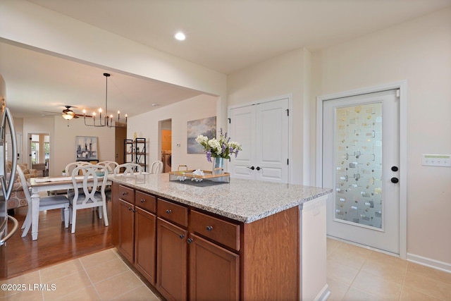 95 Sunrise Point Dr, Okatie, SC 29909 - kitchen with light tile patterned floors, light stone counters, pendant lighting, brown cabinetry, and a kitchen island