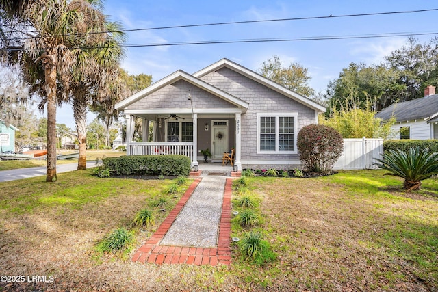 bungalow with covered porch, fence, a front lawn, and a ceiling fan