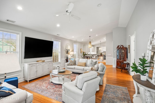 living area featuring vaulted ceiling, a wainscoted wall, light wood-type flooring, and visible vents