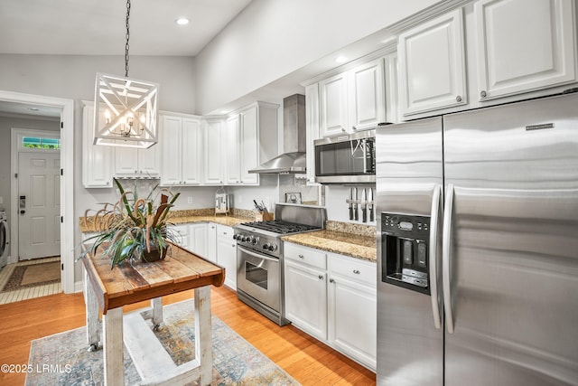 kitchen featuring appliances with stainless steel finishes, white cabinets, wall chimney range hood, and light wood finished floors