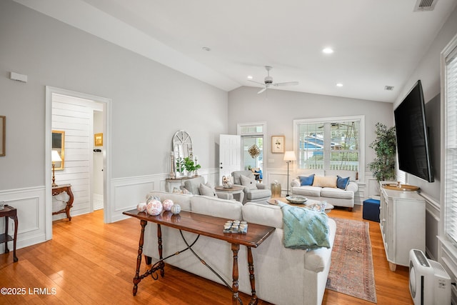 living area featuring vaulted ceiling, wainscoting, light wood-type flooring, and a ceiling fan