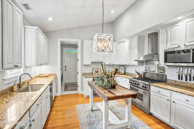 kitchen featuring white cabinets, wall chimney exhaust hood, appliances with stainless steel finishes, vaulted ceiling, and a sink