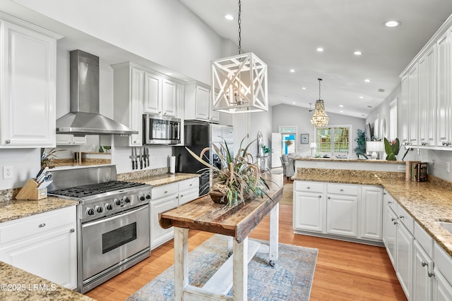 kitchen with appliances with stainless steel finishes, lofted ceiling, white cabinets, and wall chimney exhaust hood