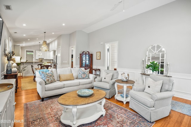 living area with vaulted ceiling, light wood-type flooring, wainscoting, and visible vents