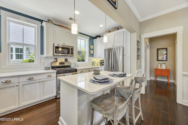 kitchen with pendant lighting, white cabinets, ornamental molding, stainless steel appliances, and dark wood-type flooring