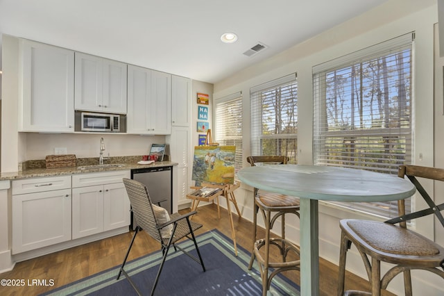 kitchen with dark hardwood / wood-style floors, stainless steel microwave, dishwasher, sink, and light stone countertops