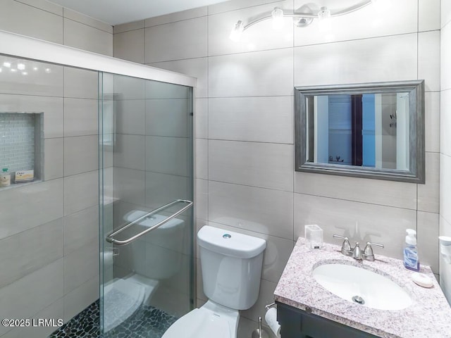 bathroom with vanity, toilet, a shower with door, and tile walls