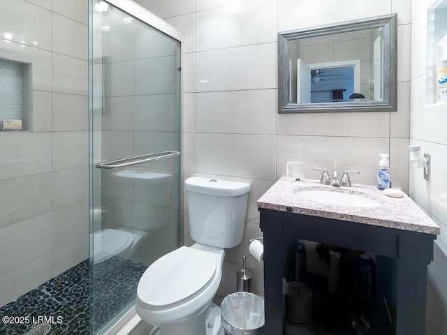 bathroom with vanity, toilet, an enclosed shower, and tile walls