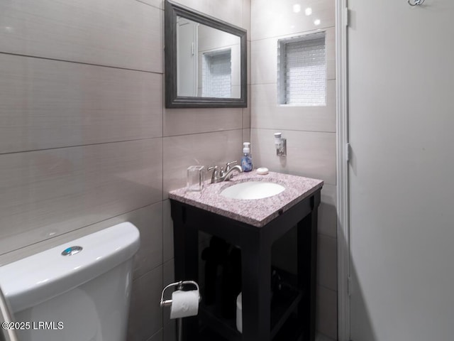 bathroom featuring vanity, tile walls, and toilet