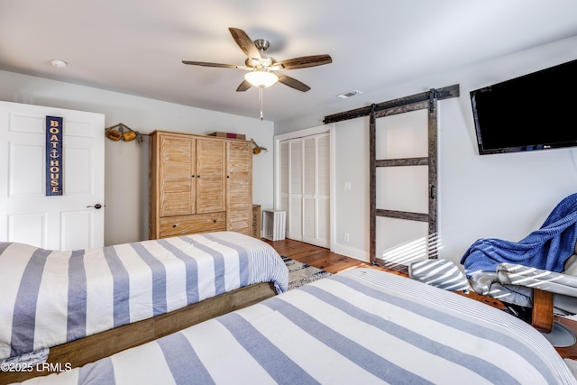 bedroom with ceiling fan, a barn door, hardwood / wood-style floors, and a closet