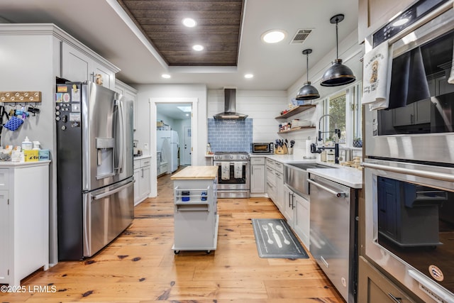 kitchen featuring appliances with stainless steel finishes, wood counters, white cabinets, a tray ceiling, and wall chimney range hood