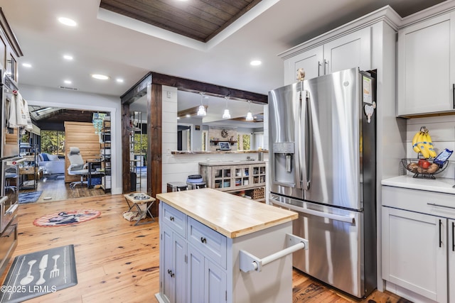 kitchen with butcher block countertops, stainless steel fridge with ice dispenser, decorative light fixtures, a raised ceiling, and light wood-type flooring