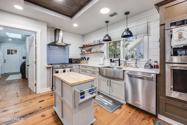 kitchen featuring decorative light fixtures, stainless steel appliances, wall chimney exhaust hood, and light wood-type flooring