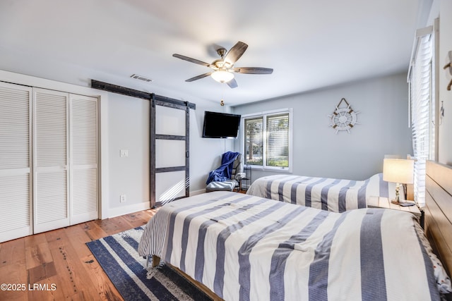 bedroom featuring a closet, a barn door, ceiling fan, and light hardwood / wood-style floors