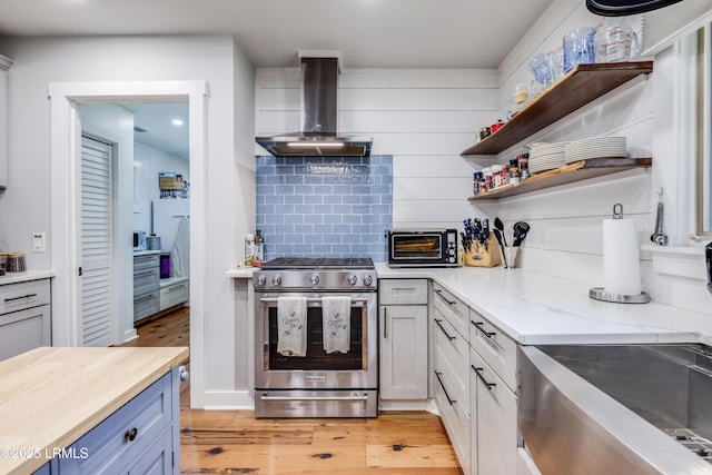 kitchen featuring wall chimney exhaust hood, butcher block countertops, gas range, light hardwood / wood-style flooring, and backsplash