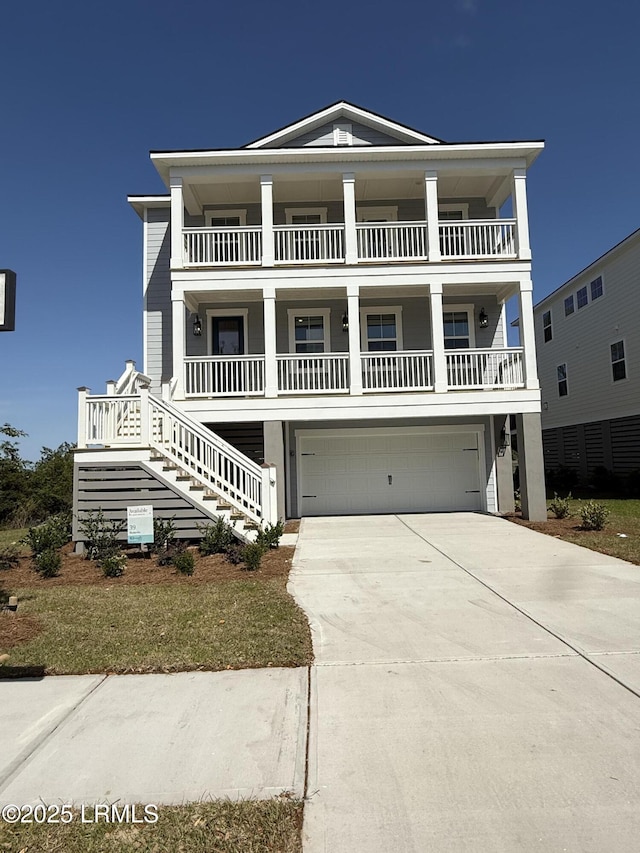 coastal home featuring stairway, an attached garage, a balcony, and driveway