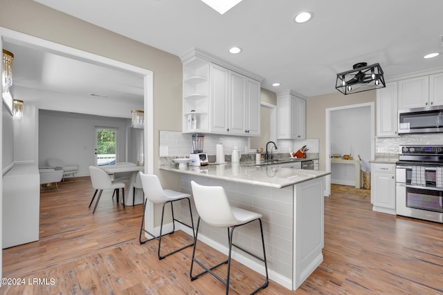 kitchen featuring white cabinetry, a kitchen bar, kitchen peninsula, and appliances with stainless steel finishes