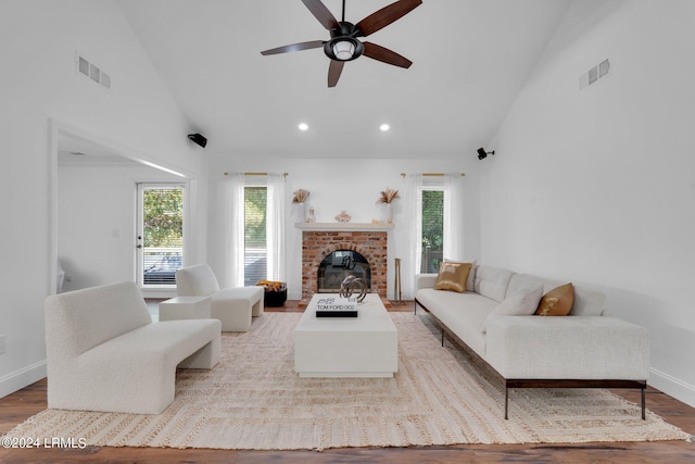 living room with ceiling fan, high vaulted ceiling, light hardwood / wood-style floors, and a brick fireplace