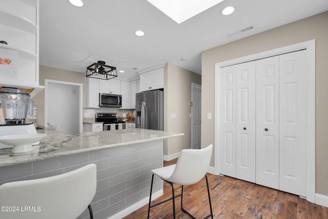 kitchen with white cabinetry, a skylight, stainless steel appliances, dark hardwood / wood-style floors, and kitchen peninsula