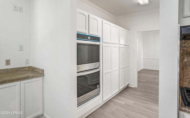 kitchen with ornamental molding, double oven, dark stone counters, light hardwood / wood-style floors, and white cabinets