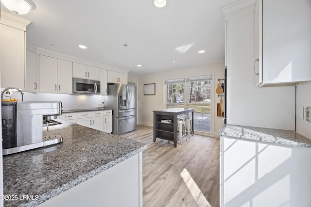 kitchen featuring tasteful backsplash, light wood-style flooring, appliances with stainless steel finishes, dark stone countertops, and white cabinetry